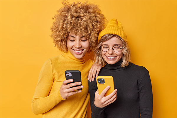 indoor-shot-happy-beautiful-women-enjoy-mobile-offer-browse-new-application-website-being-addicted-modern-technologies-holds-cellulars-chat-online-isolated-vivid-yellow-background